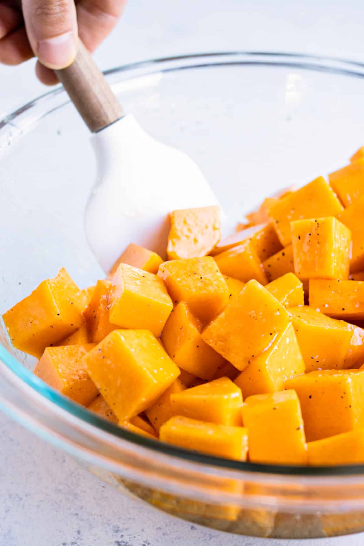 Butternut squash cubes are mixed together in a bowl with oil and seasonings.