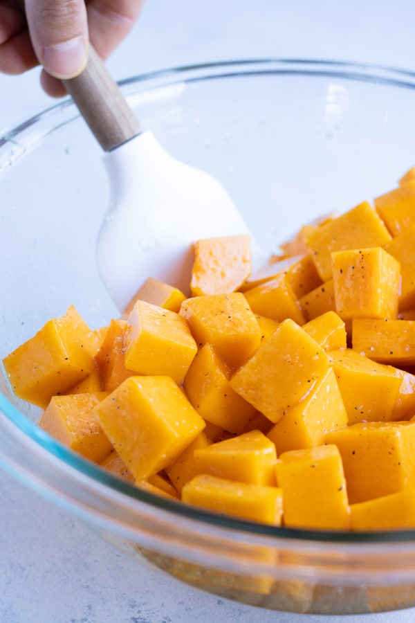 Cubed butternut squash is tossed in the oil.