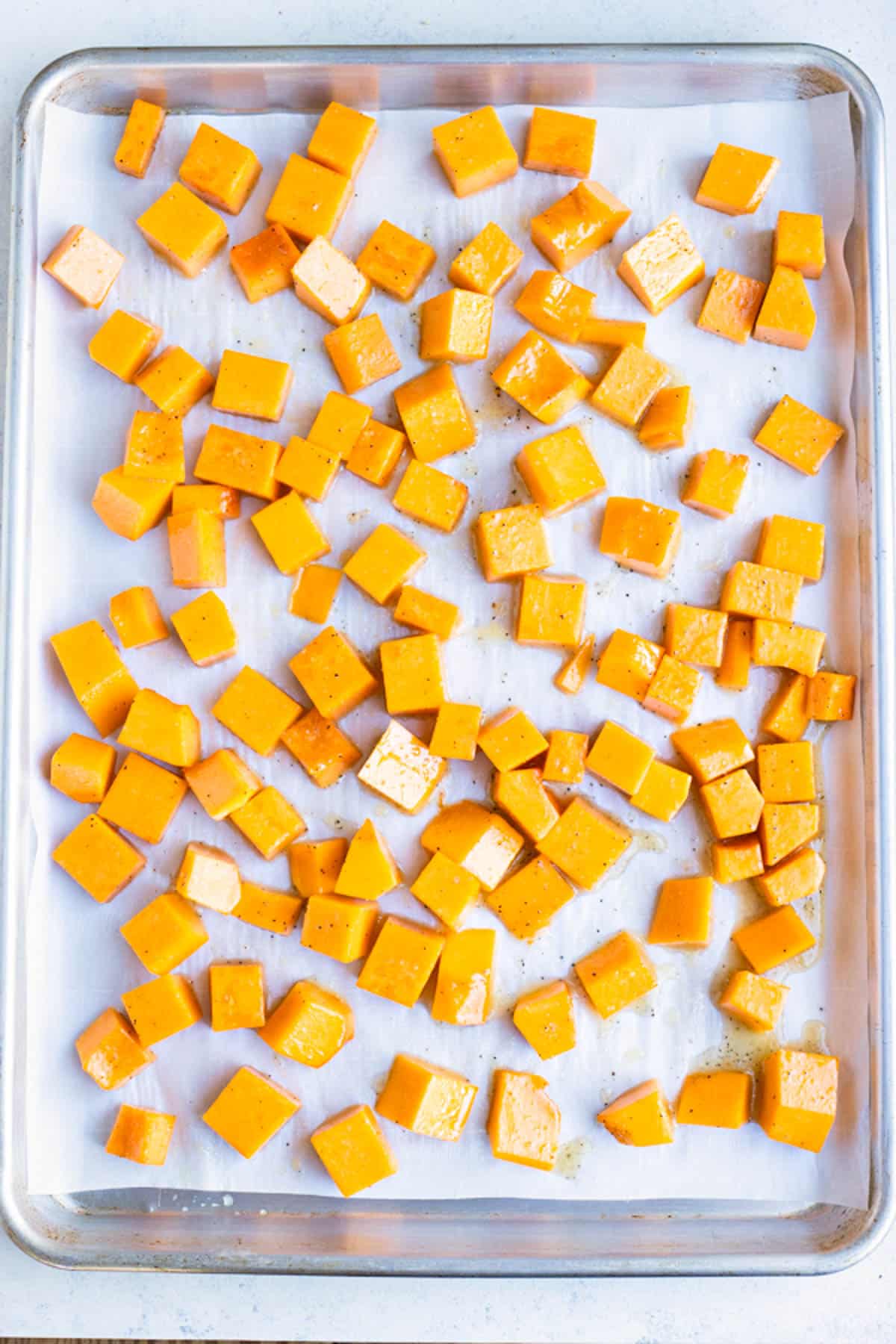 Butternut squash cubes are roasted on a sheet pan.