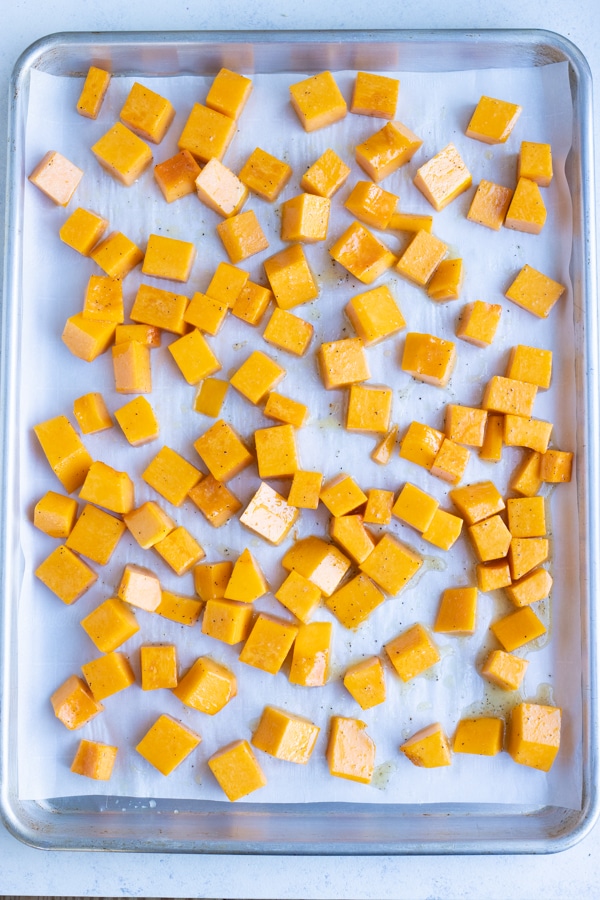 Cubed butternut squash is roasted in the oven on a baking sheet.