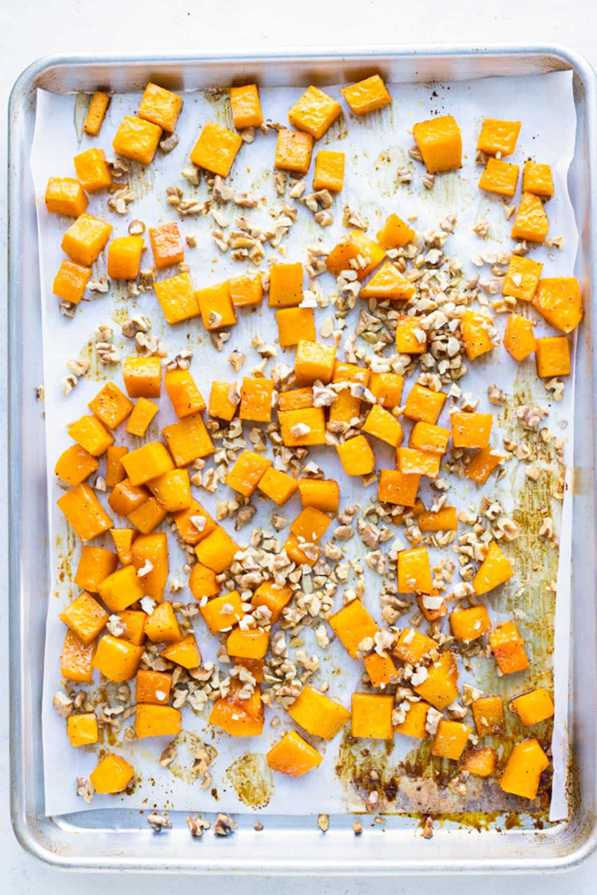 Roasted butternut squash cubes and walnuts are on a baking sheet with parchment paper.