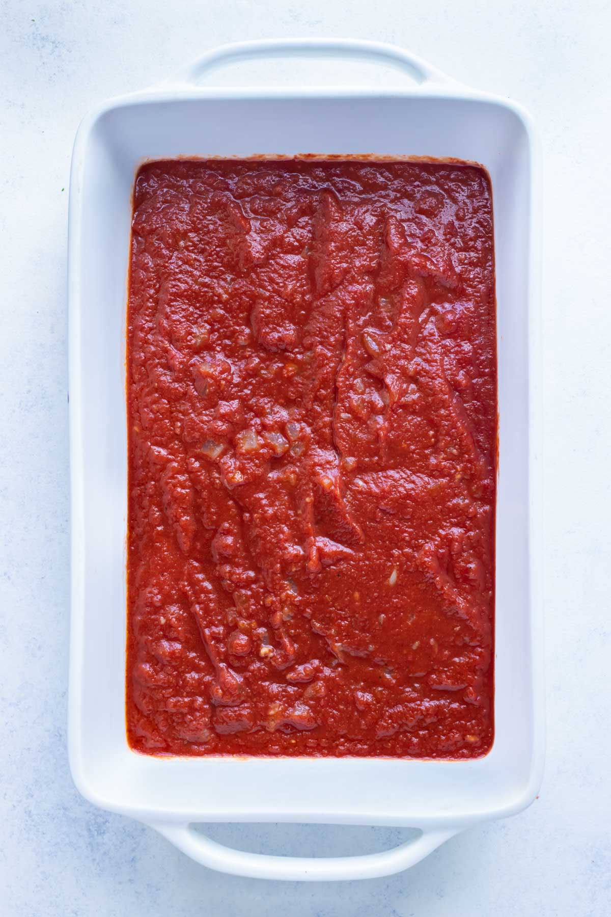Sauce is layered in the bottom of the casserole dish.