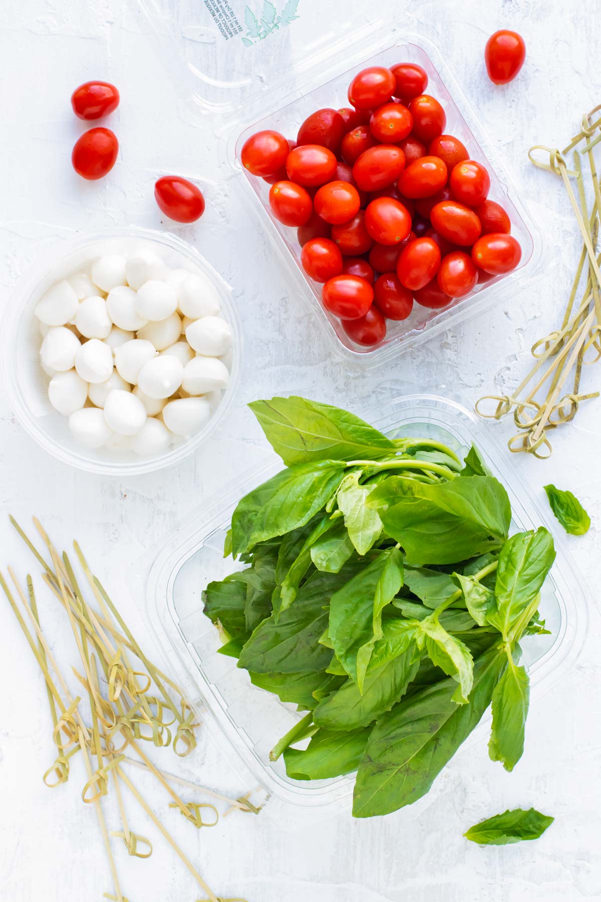 A pint full of cherry tomatoes, mozzarella pearls, and fresh basil leaves as the ingredients for caprese skewers.