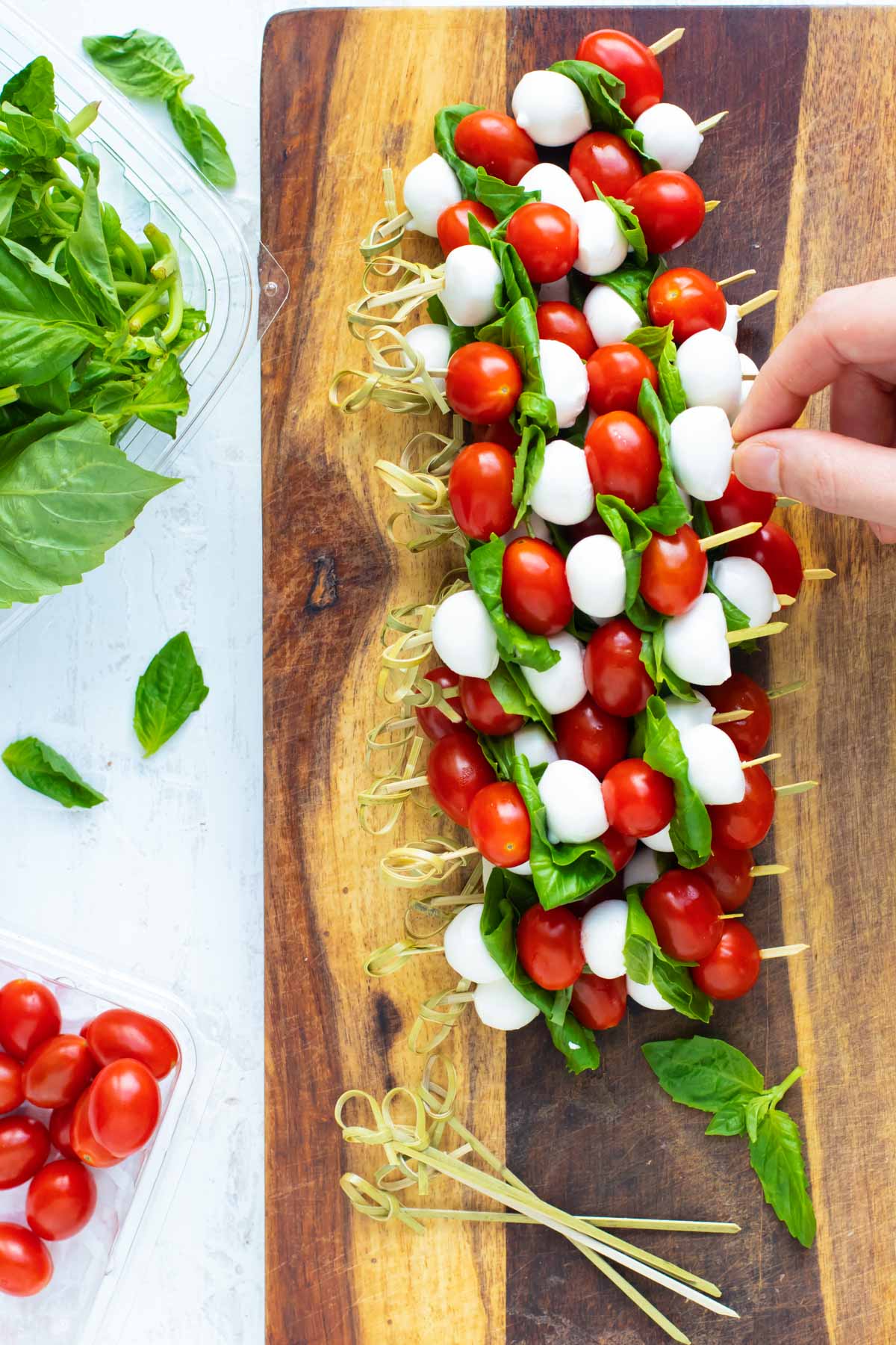 A hand picking up a caprese skewer from a wooden cutting board.