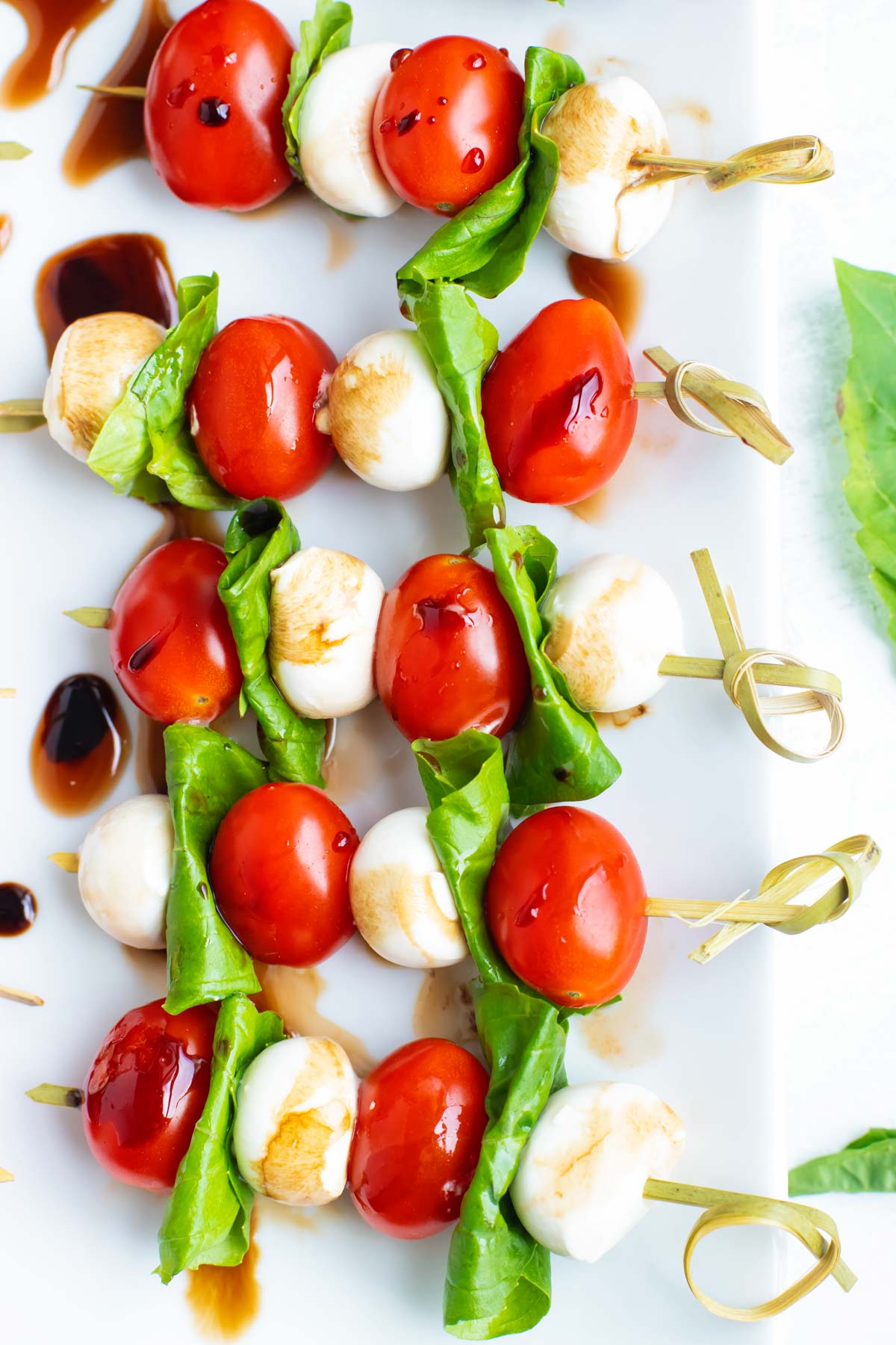 Caprese skewers on a white plate with a drizzle of balsamic glaze.