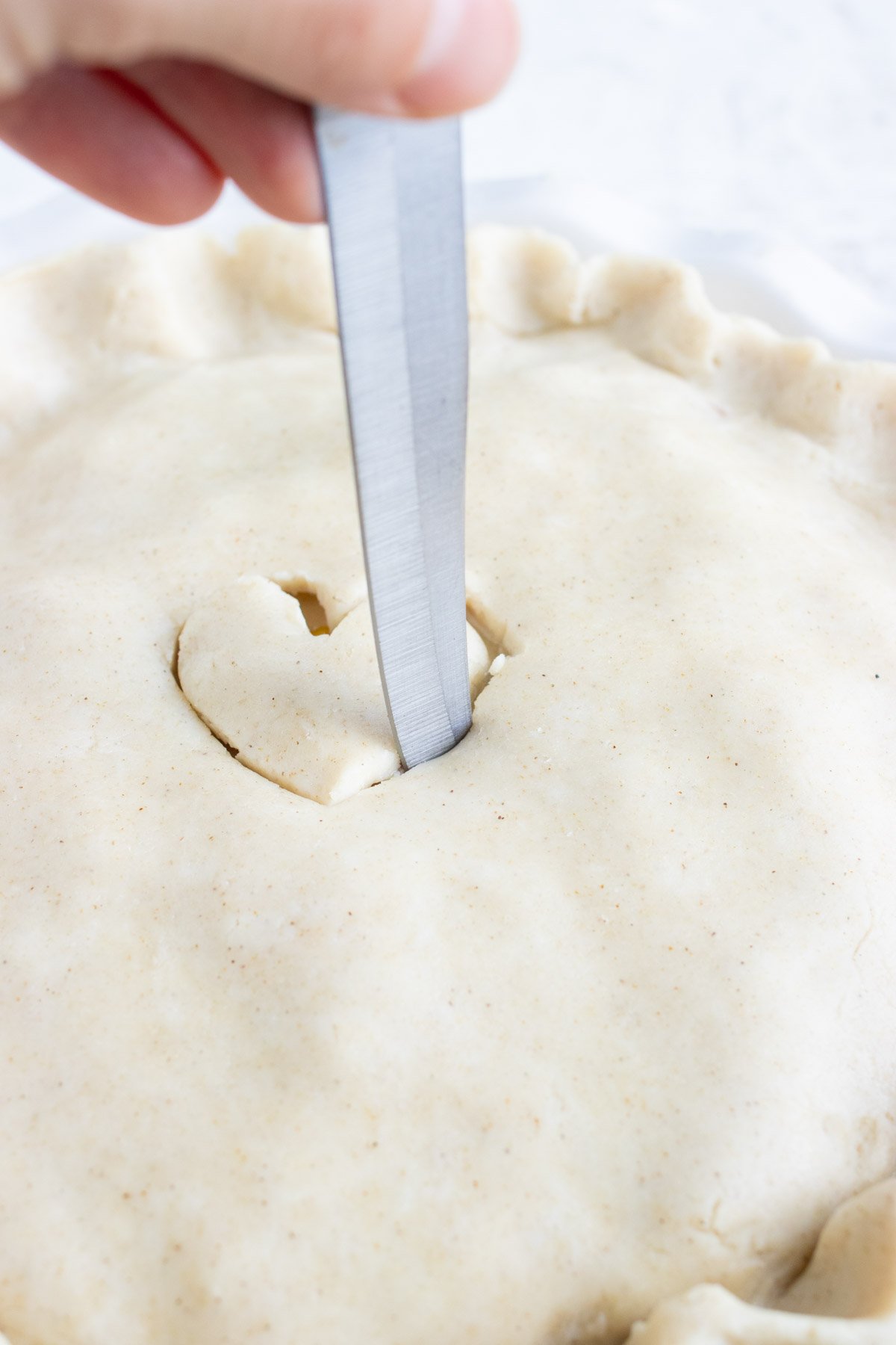 A knife is used to cut out a heart on the top pie crust.
