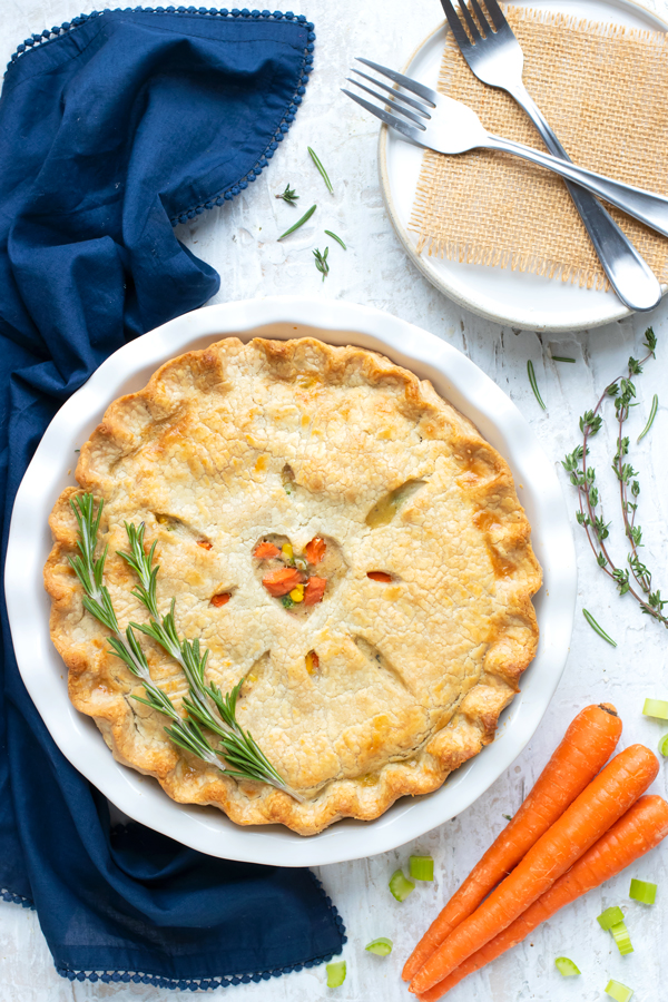 A whole turkey pot pie is set on the counter near plates and forks.