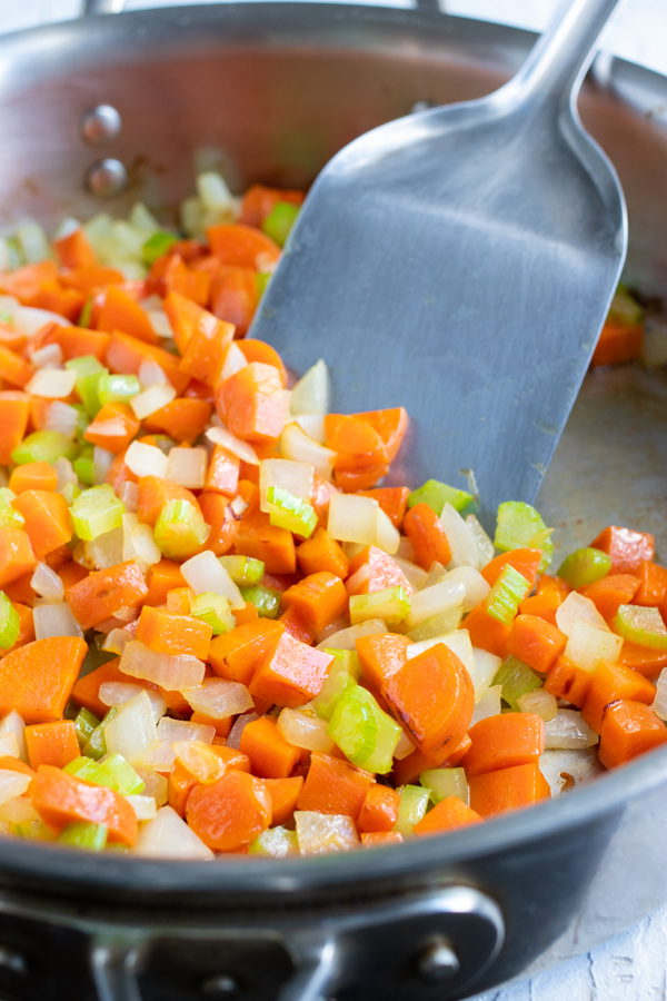 Carrots, celery, and onion are sautéed on the stove.