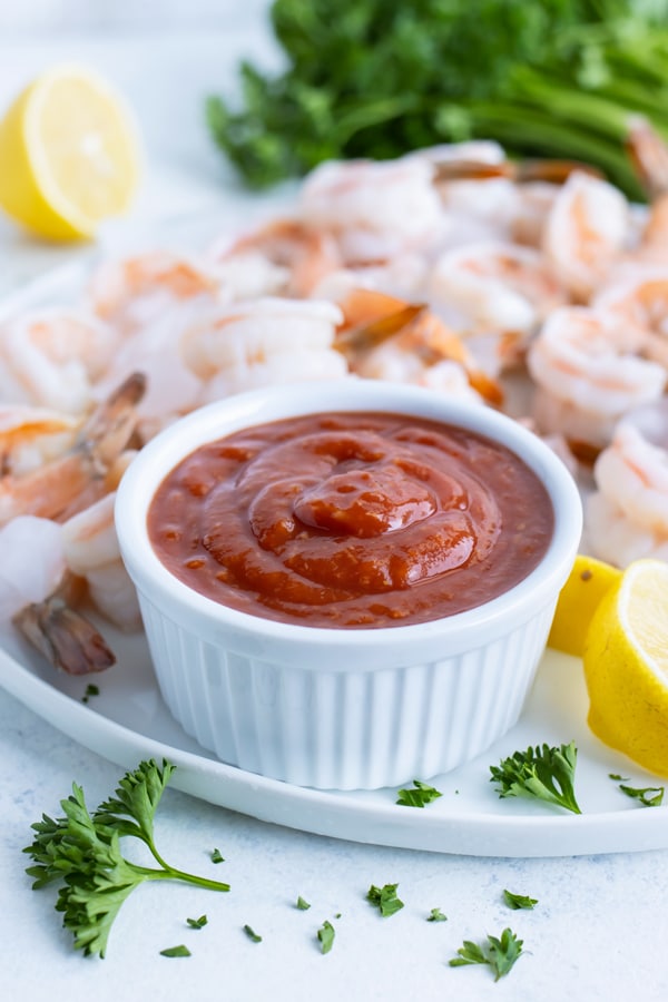 A cup of homemade cocktail sauce is served on a platter with shrimp.