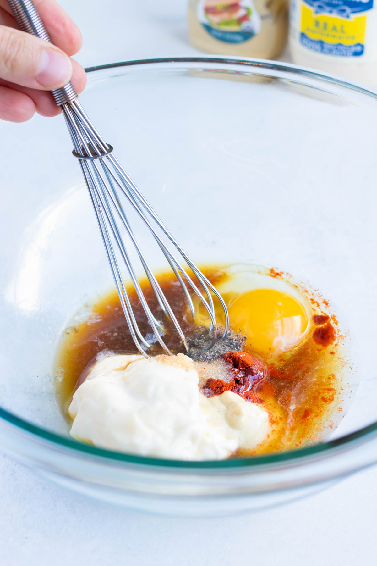 Egg, mayonnaise, worcestershire sauce and other wet ingredients are whisked together in a bowl.