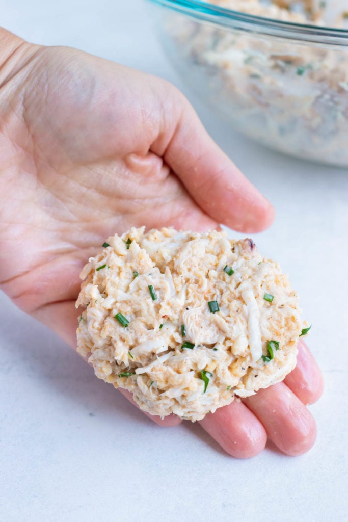 A hand is holding a jumbo lump crab cake before cooking.