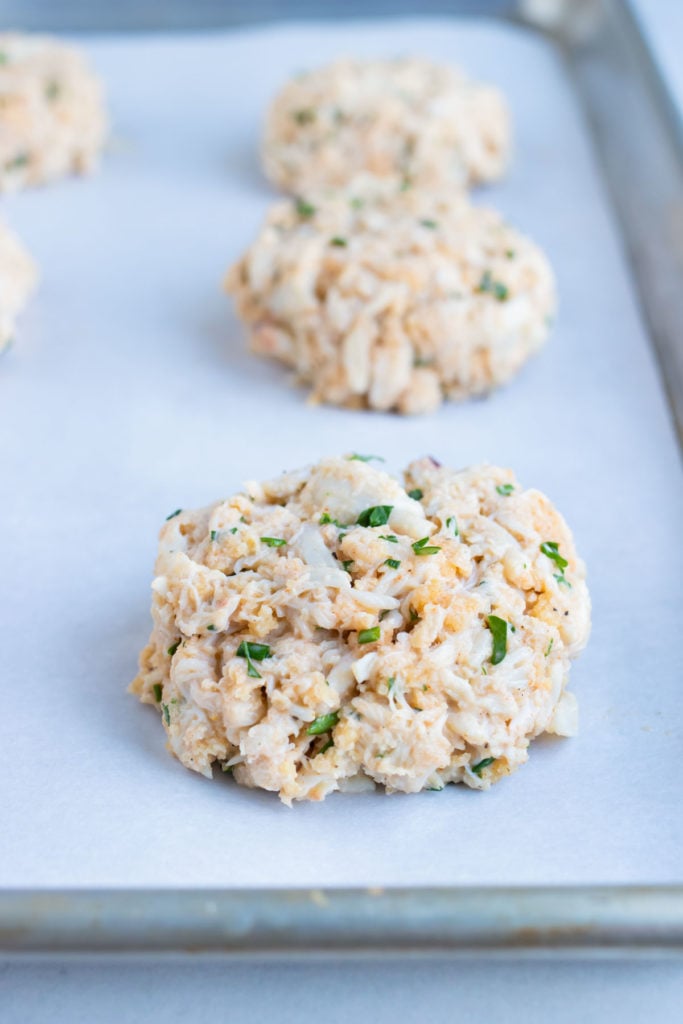 Crab cakes are shaped and laid on a baking sheet before cooking.