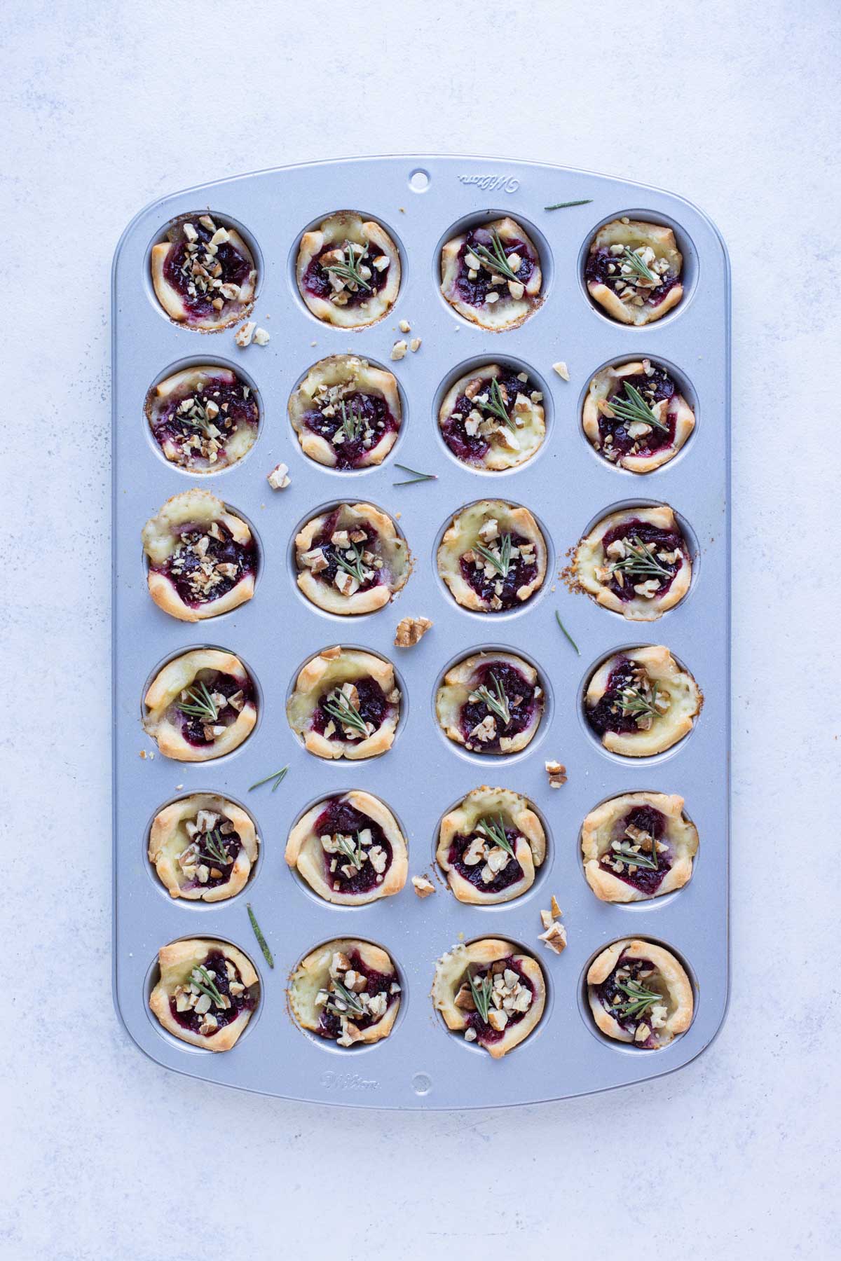 Baked brie bites are topped with toasted pecans and rosemary.