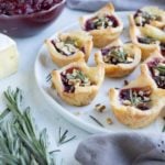 A plate of brie and cranberry filled puff pastry bites are shown on the counter.