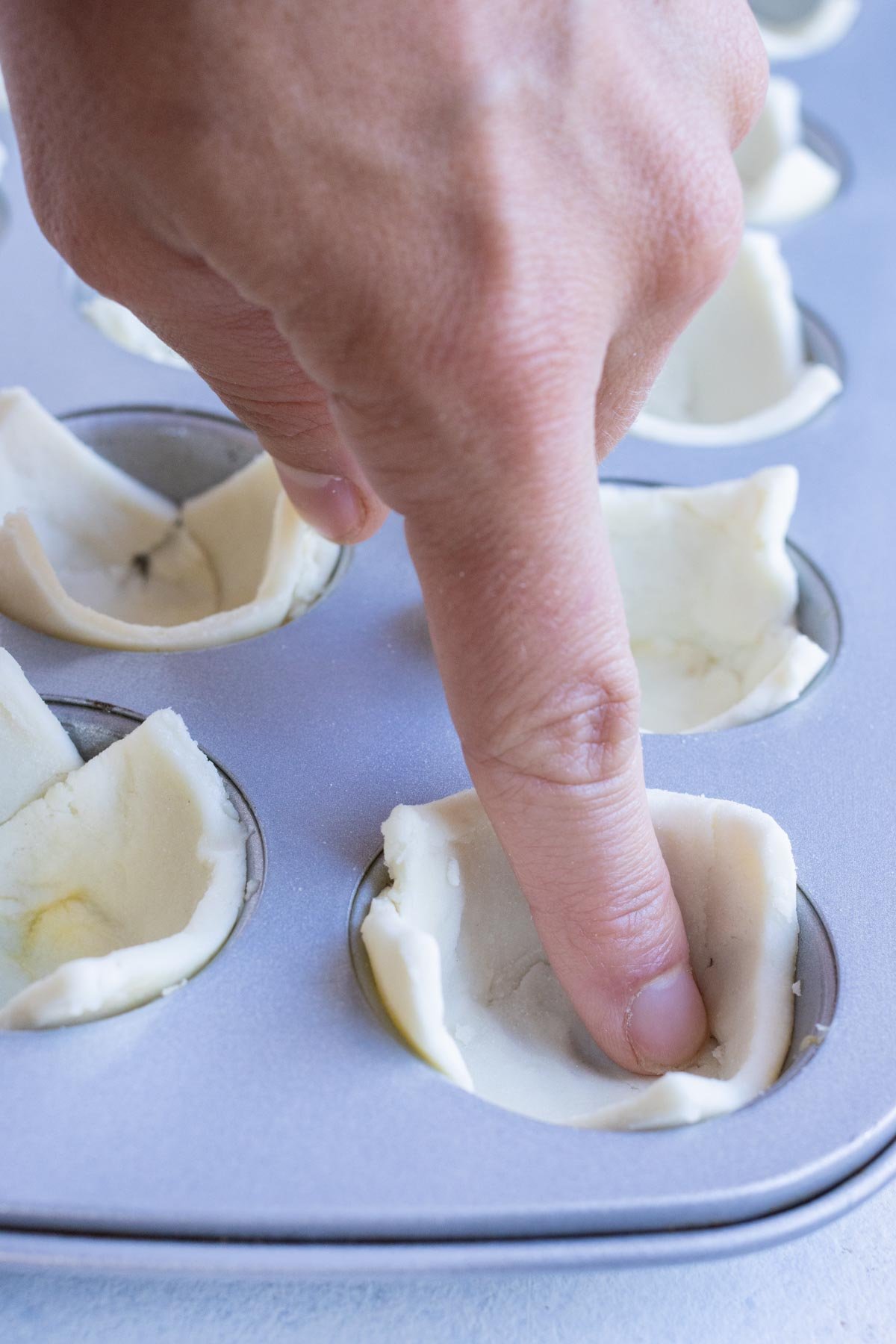 A mini muffin pan is filled with the puff pastry squares.