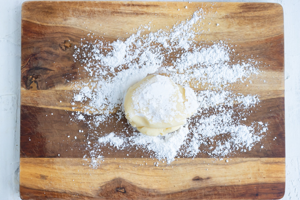 Ball of dough on a wooden surface dusted with powdered sugar.