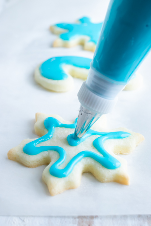 Icing being piped onto a sugar cookie in the shape of a snowflake.