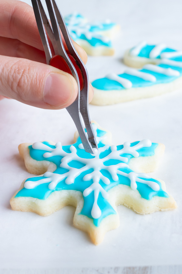 A hand holding tweezers dropping pearls onto a cookie.