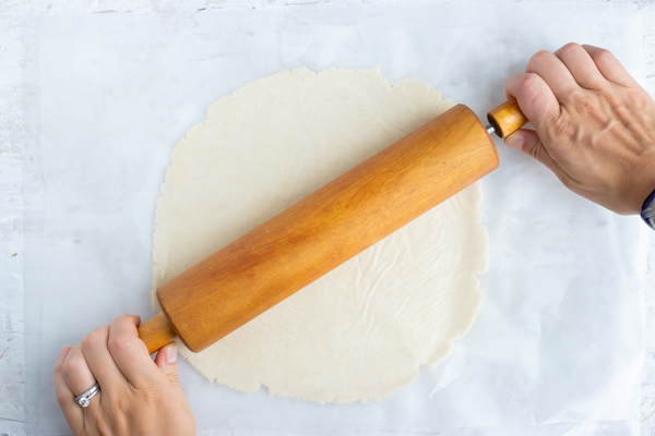 Homemade pie crust is rolled out on parchment paper. 