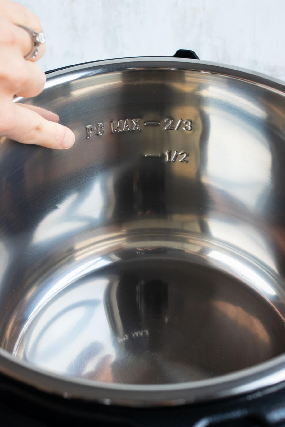 A finger pointing to the max fill line on the inside of an Instant Pot.