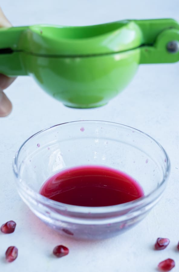 Pomegranate seeds are juiced into a bowl.