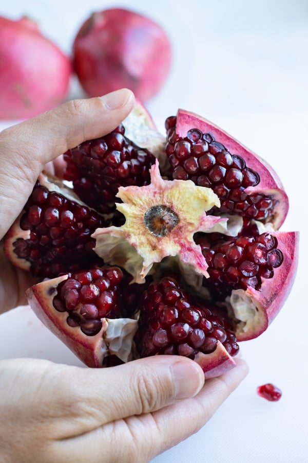 Two hands are used to separate the pomegranate sections.