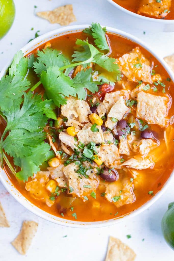 A white bowl of pressure cooker chicken tortilla soup topped with cilantro, avocado, and tortilla chips.
