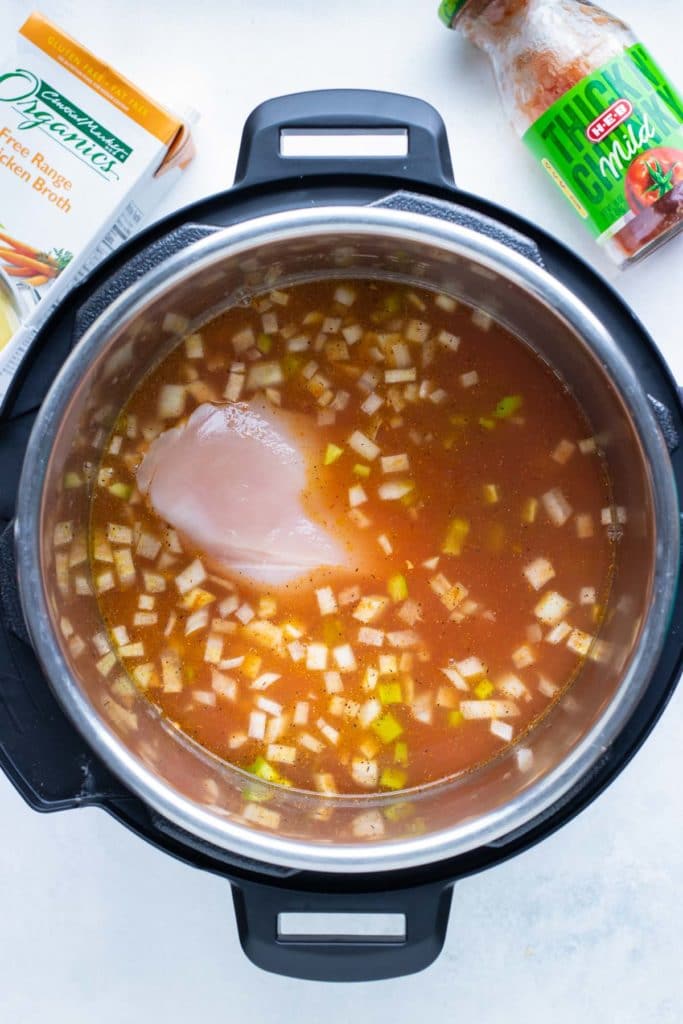 Chicken breasts submerged in salsa broth with corn in an Instant Pot for easy chicken tortilla soup.
