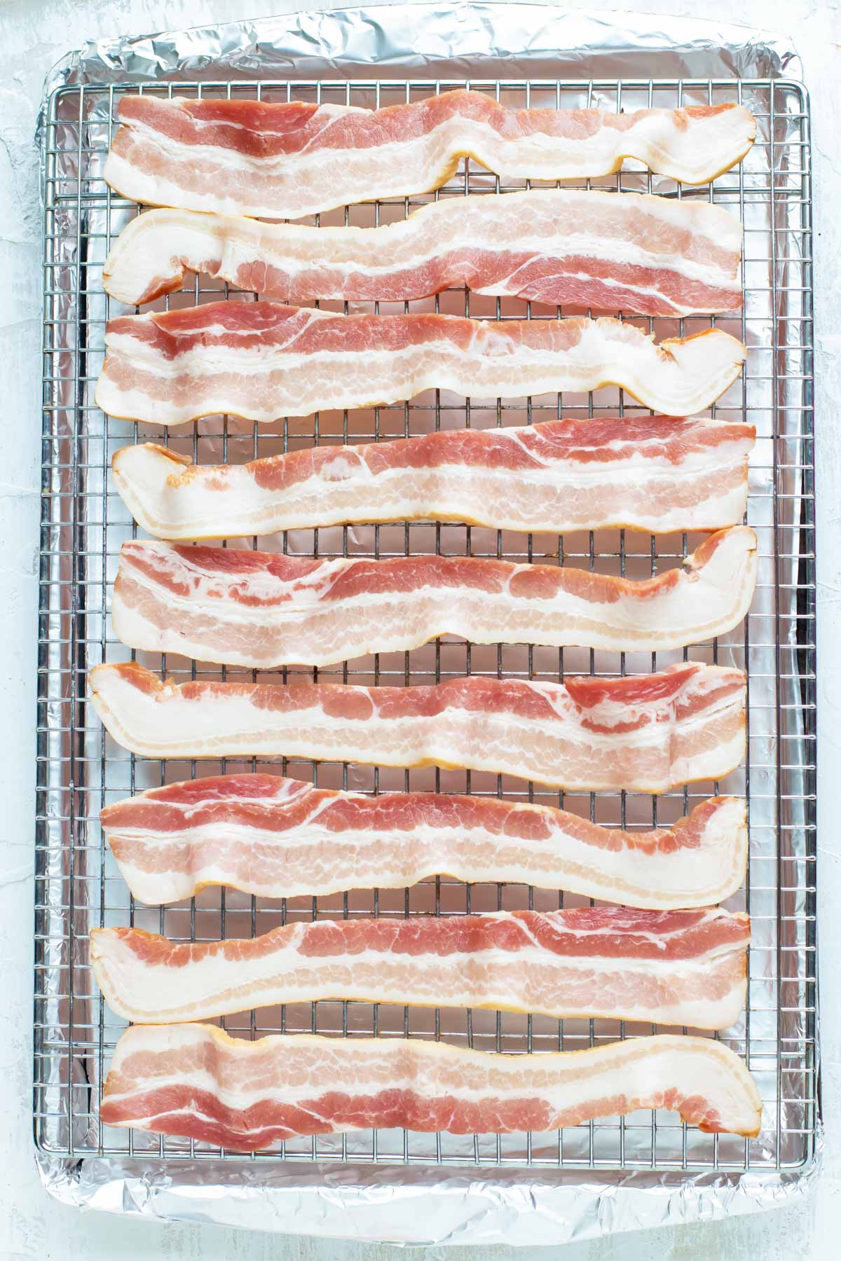A sheet pan full of bacon strips with a wire rack.