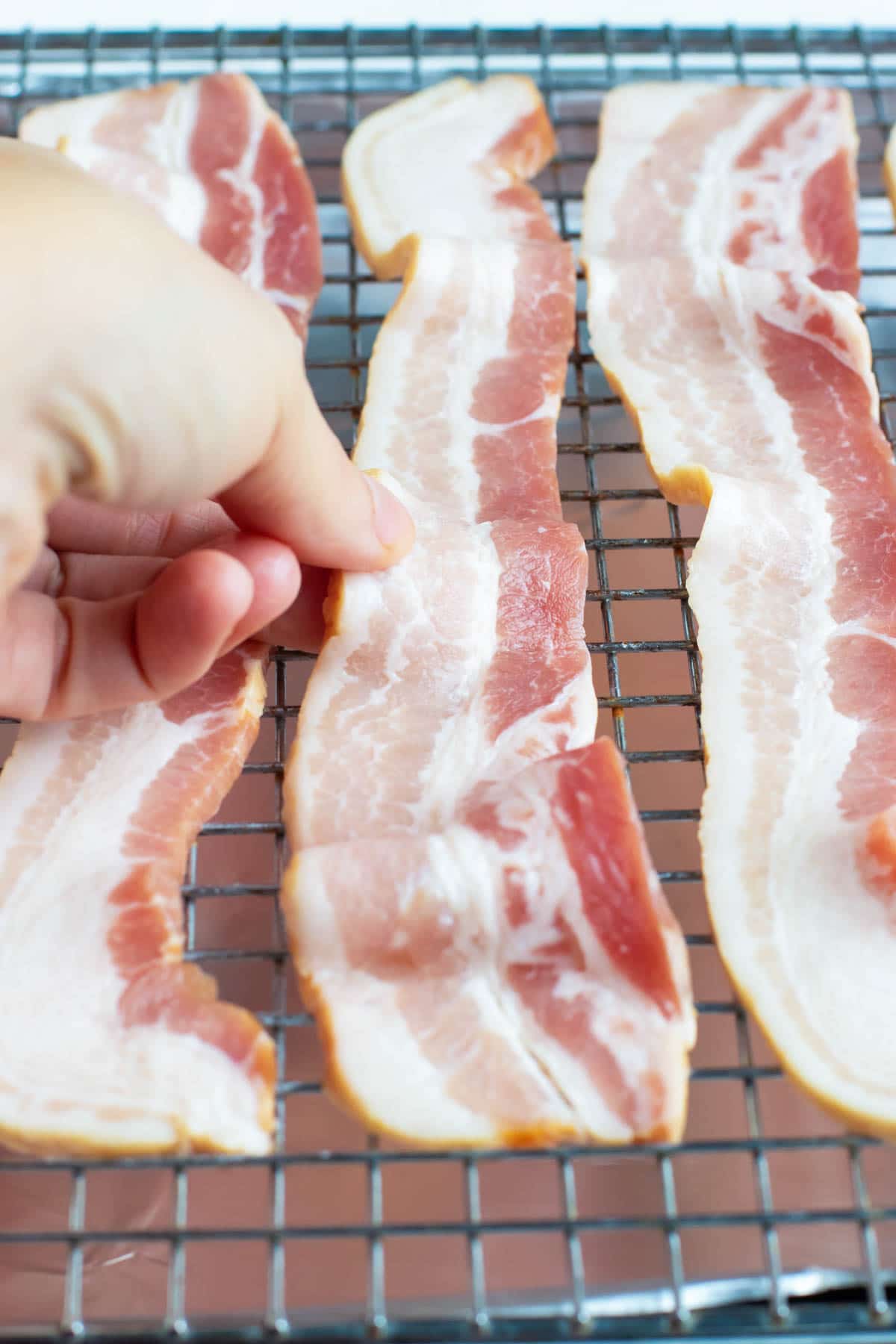 A hand roling a piece of bacon and showing how to cook bacon in the oven.