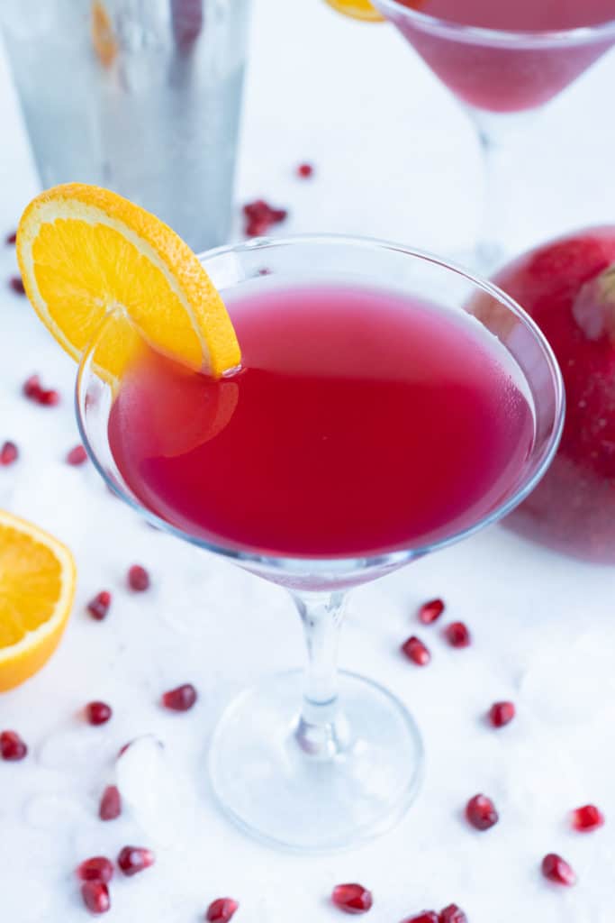 Orange slice is added to the martini glass full of a pomegranate martini.