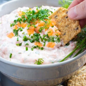 A hand scooping salmon dip with a cracker.