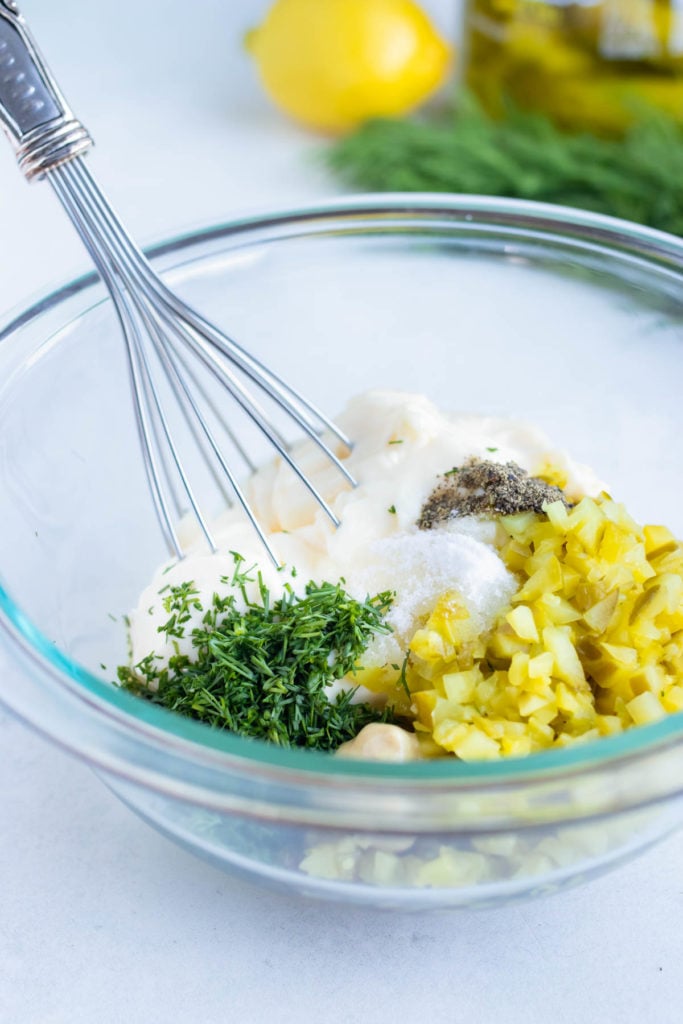 All the tartar sauce ingredients whisked together in a glass bowl.