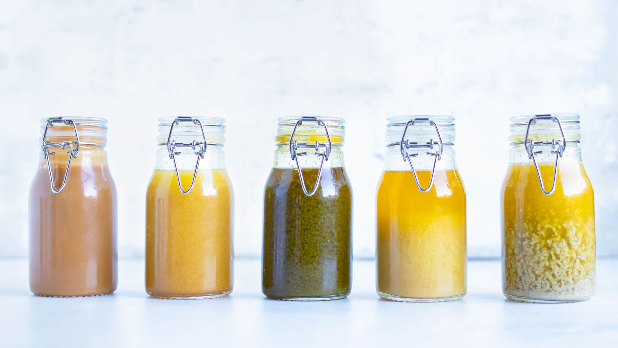 Five glass jars full of healthy homemade salad dressing recipes.