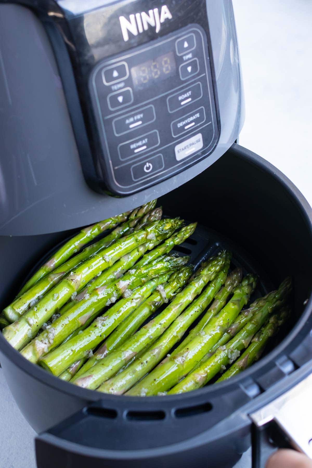 Prepped asparagus is placed in the air fryer for cooking.
