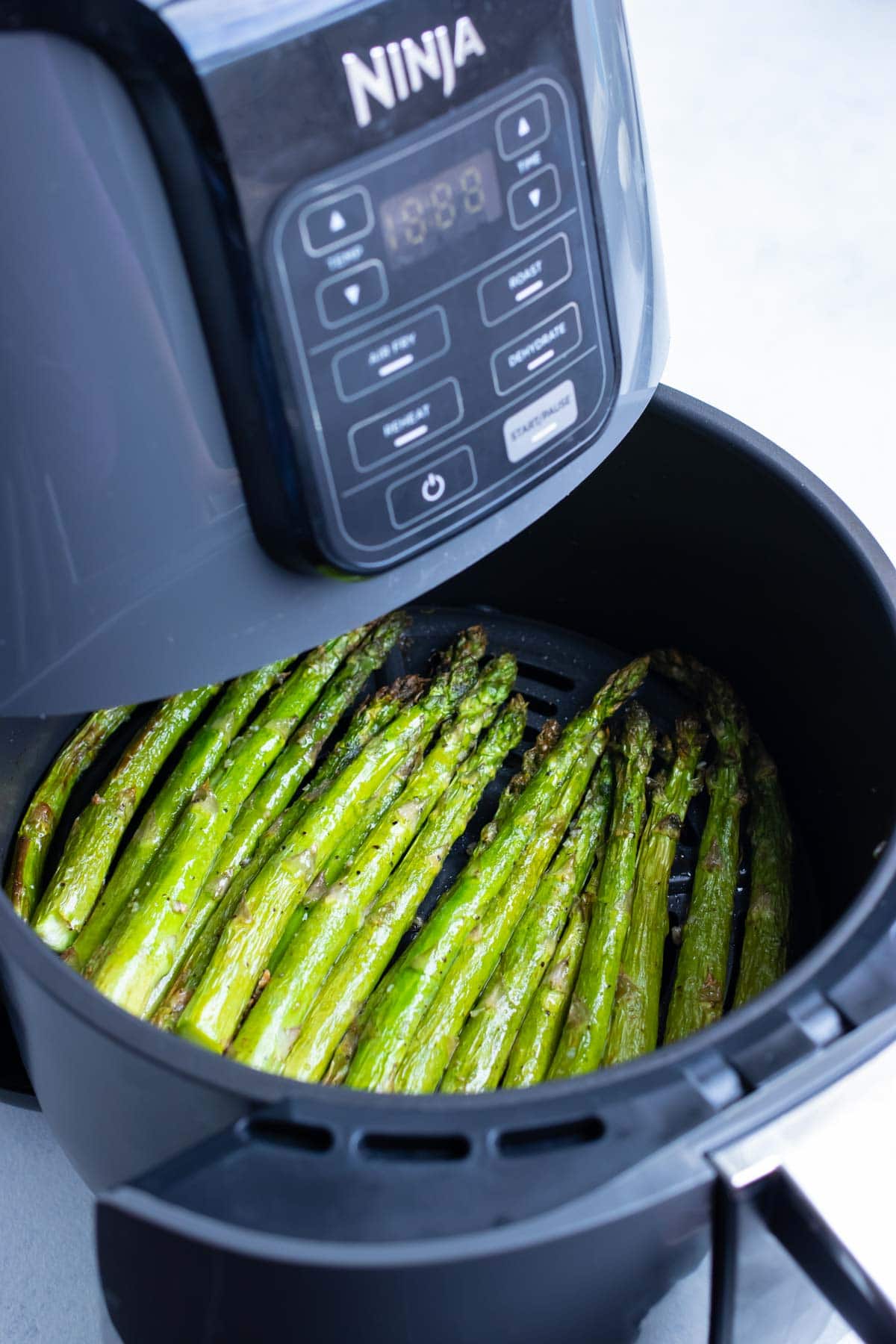 Air fryer is opened to show crisp air fryer asparagus
