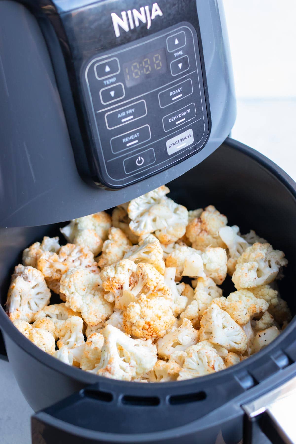 Seasoned cauliflower florets are placed in the air fryer.