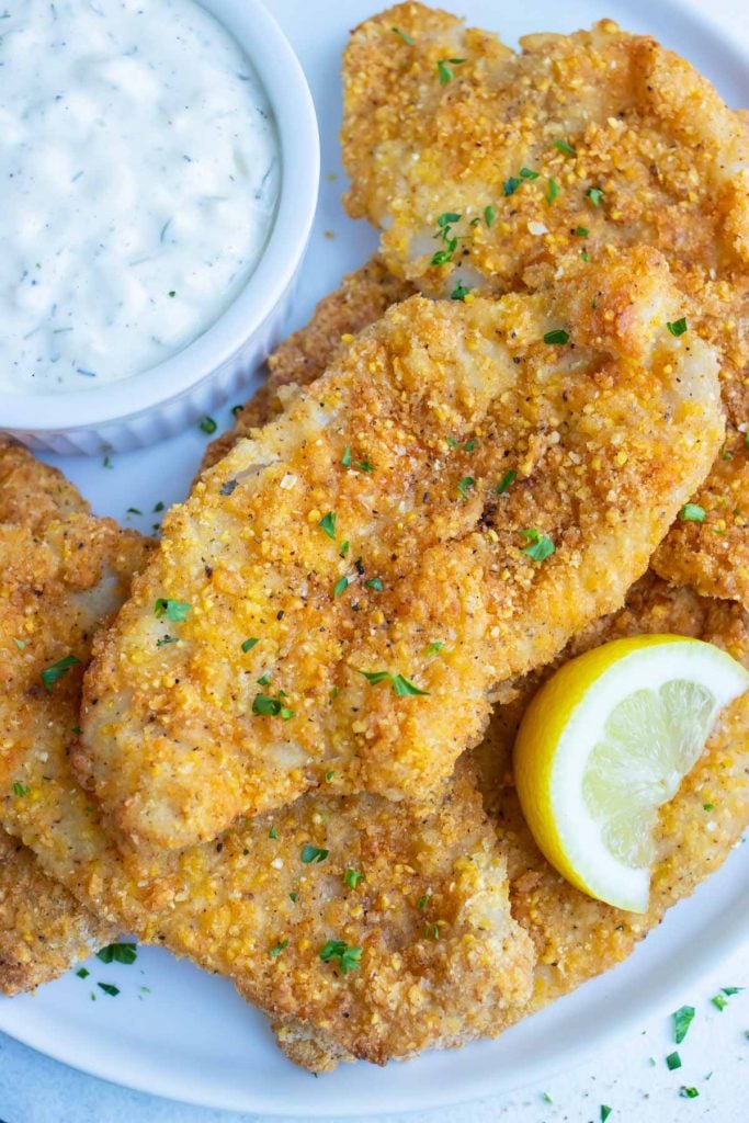 Crispy air fryer fish is served on a white plate with fresh lemon and tartar sauce.