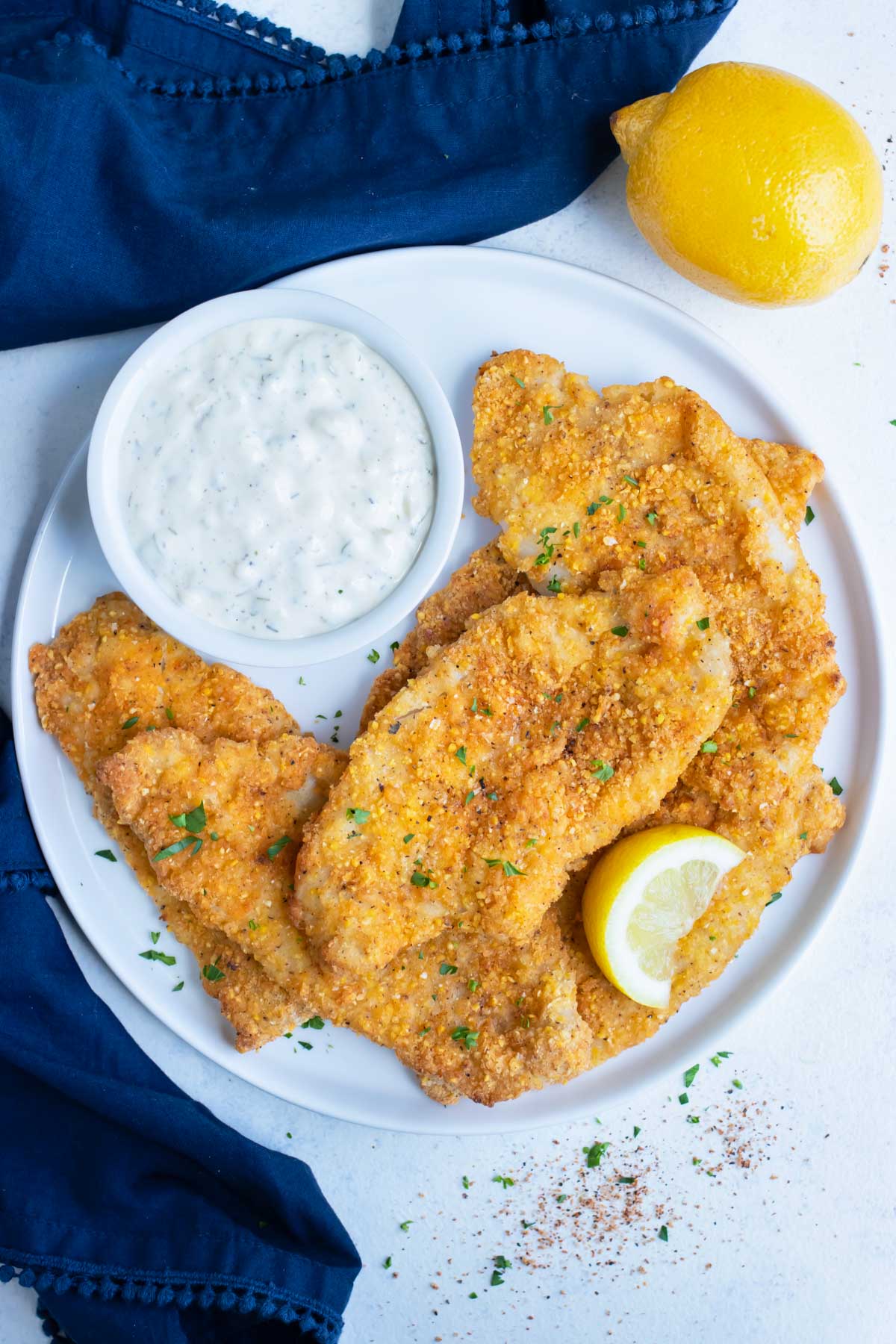 An overhead shot shows air fryer fish served on a white plate with tartar sauce.