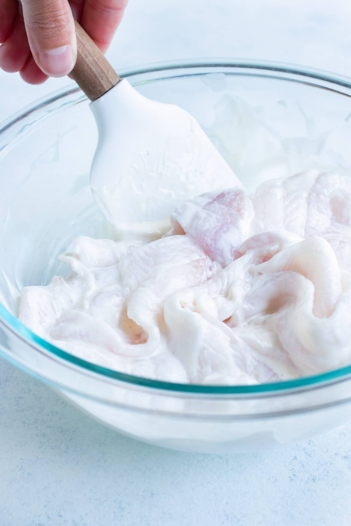 The fish is coated in mayonnaise in a glass bowl.