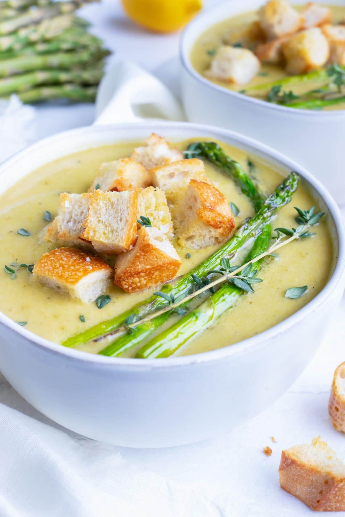 A white serving bowl full of a creamy asparagus soup recipe with roasted asparagus spears and homemade croutons.