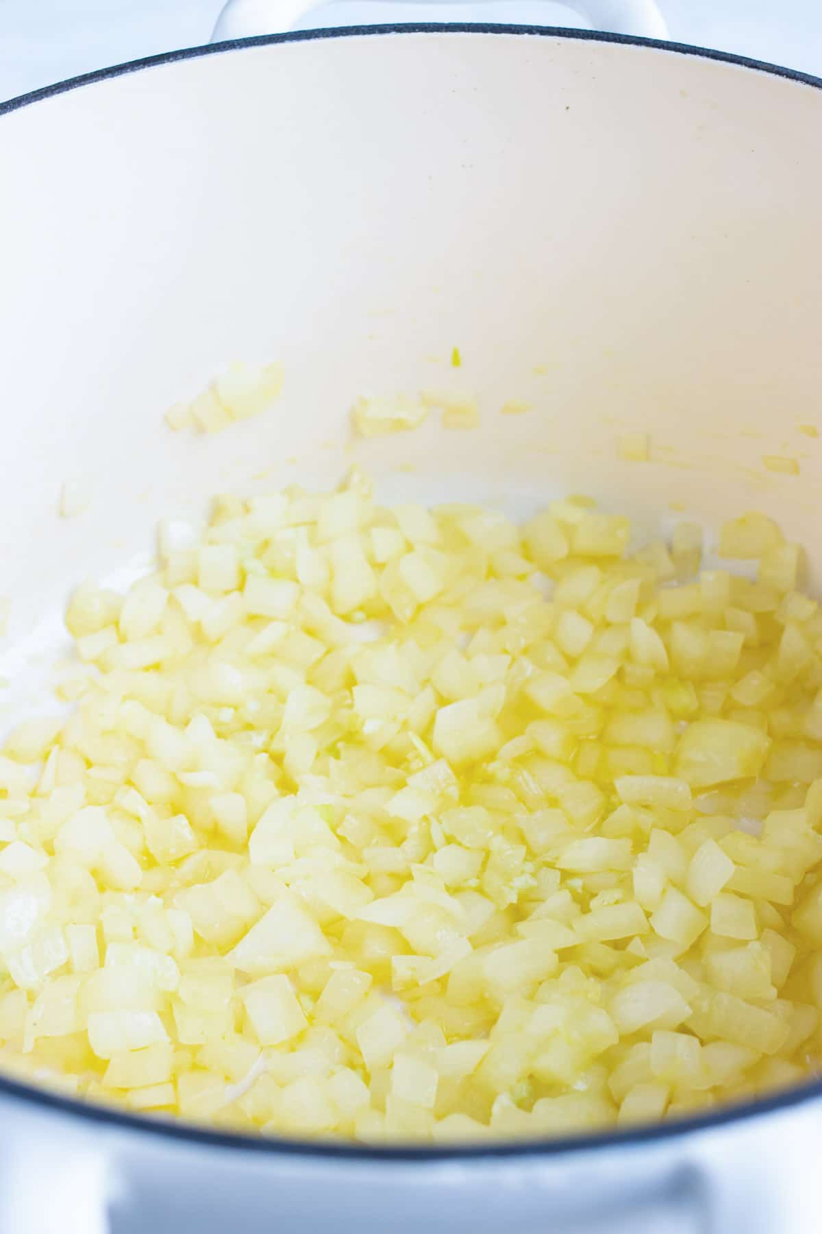 Onions sautéing in a white dutch oven.