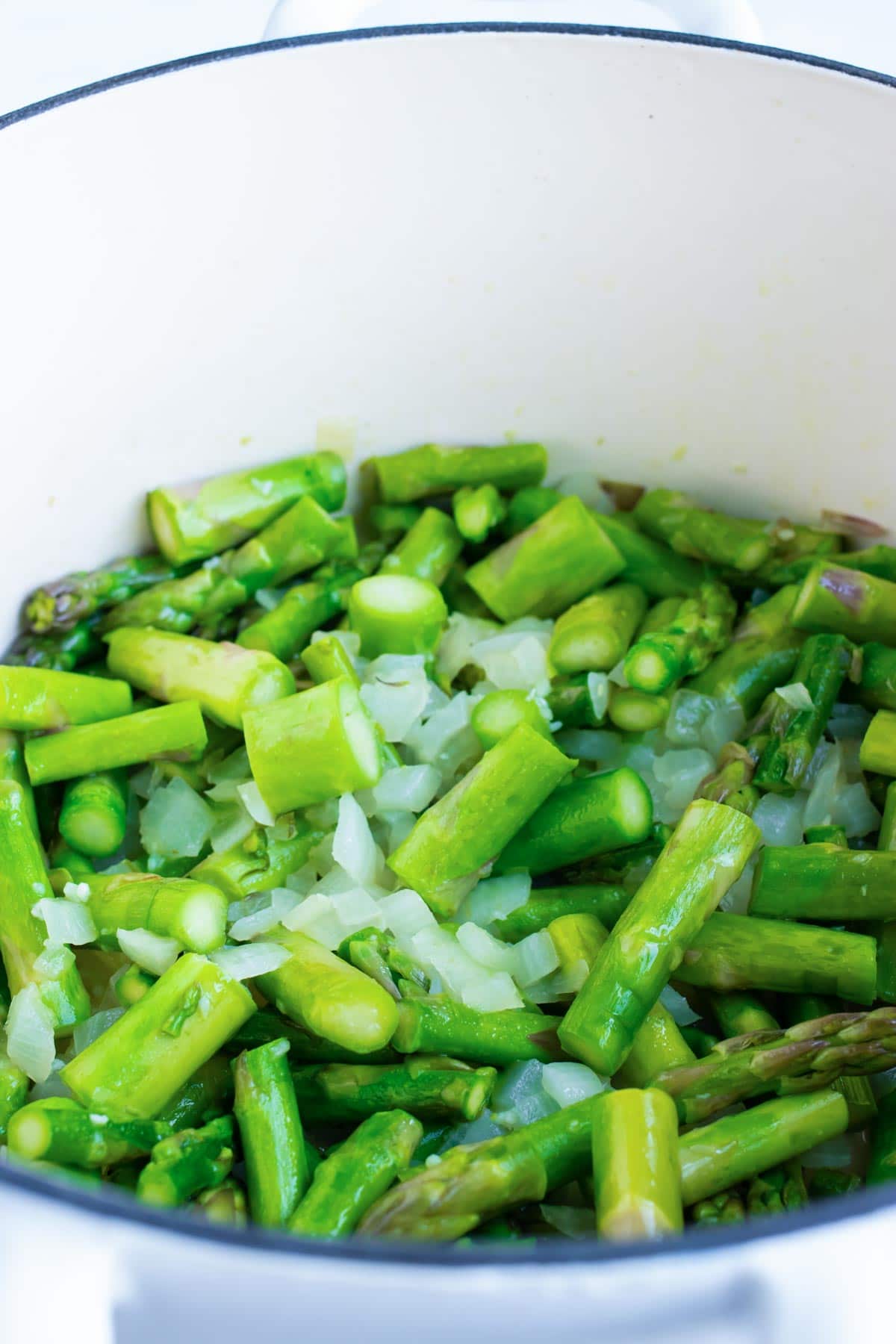 Asparagus and onions cooking in a white dutch oven.