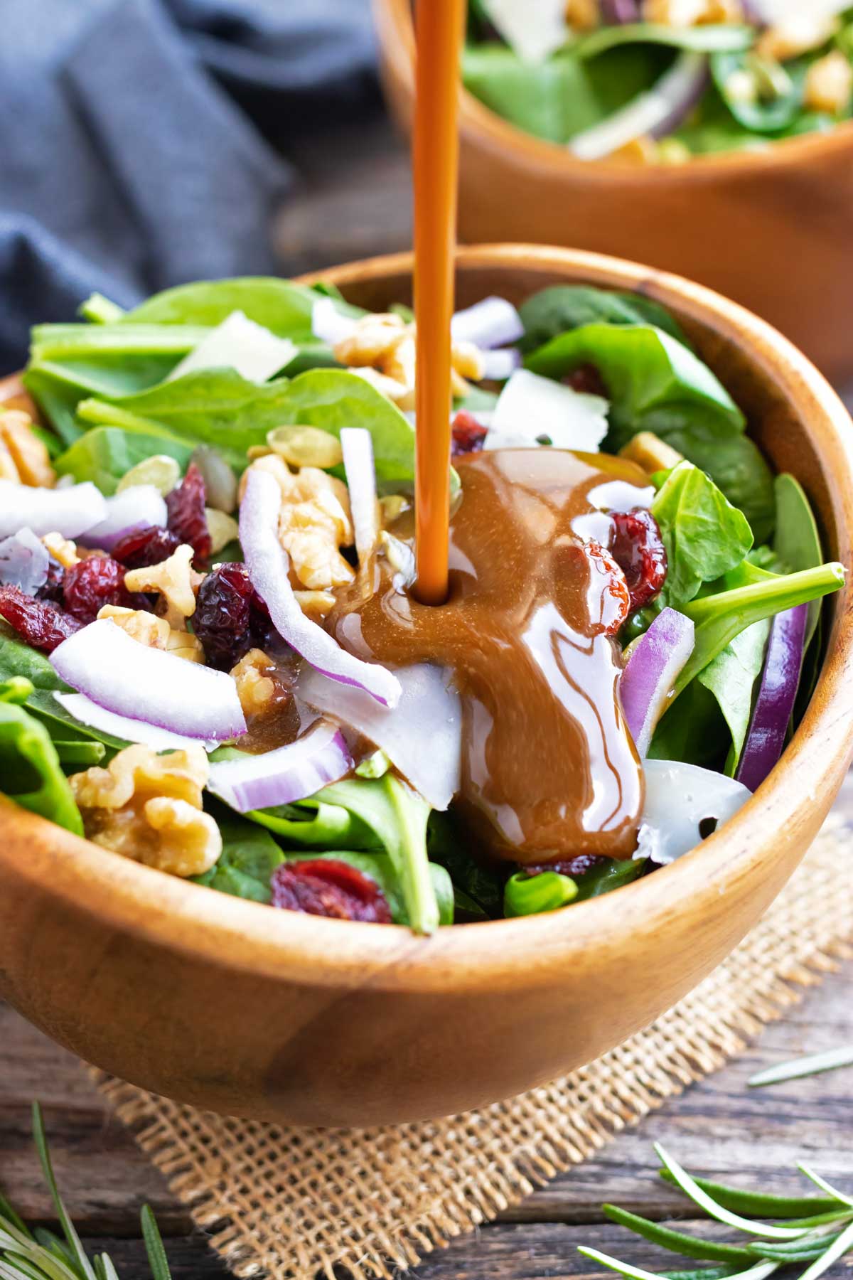A healthy and easy balsamic vinaigrette dressing being poured onto a spinach salad with cranberries.