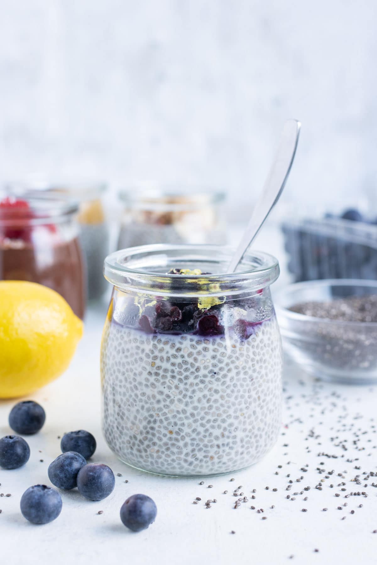 Lemon blueberry flavored chia seed pudding is shown in a jar with a spoon.