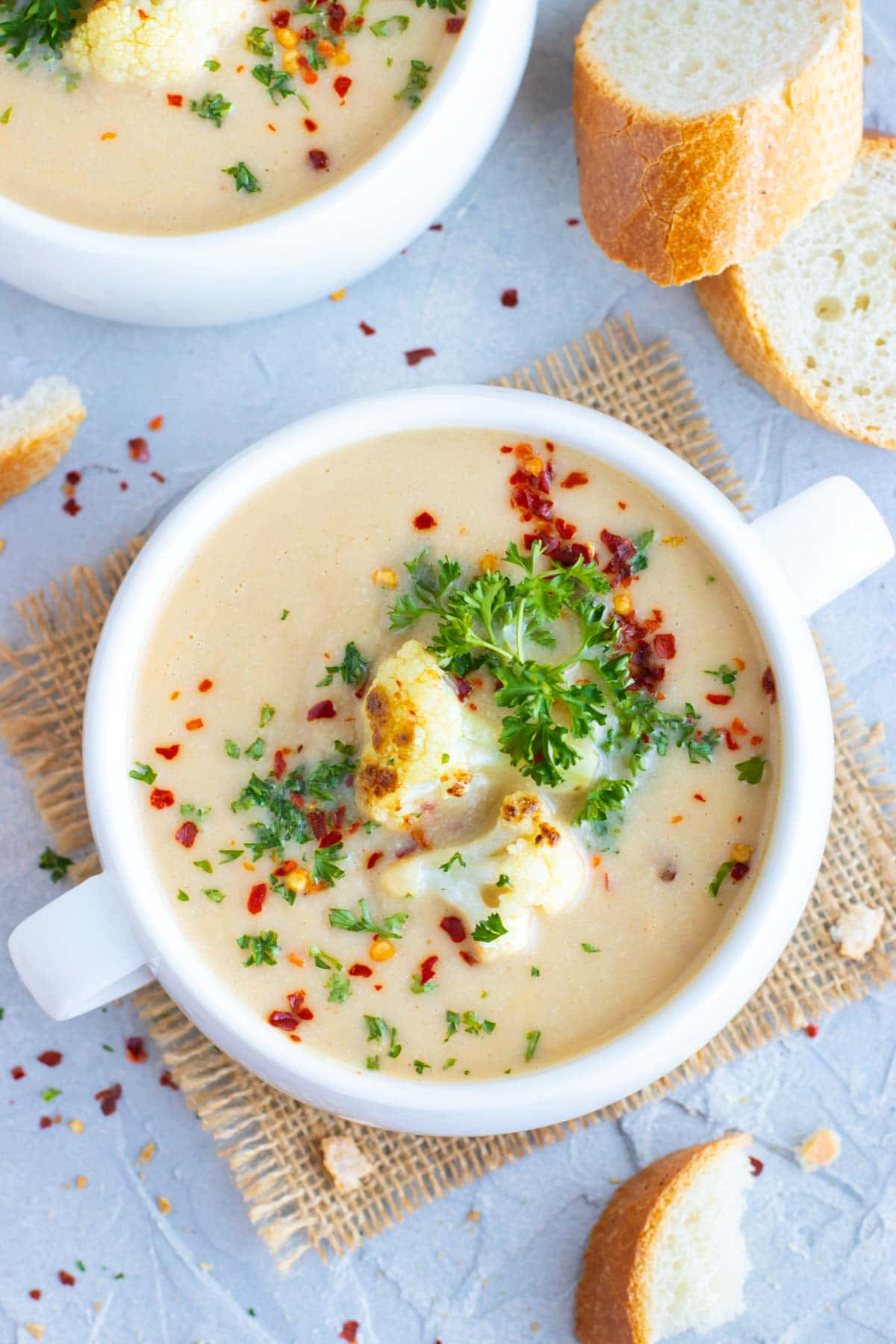 Two bowls full of a cauliflower soup recipe next to a head of cauliflower.