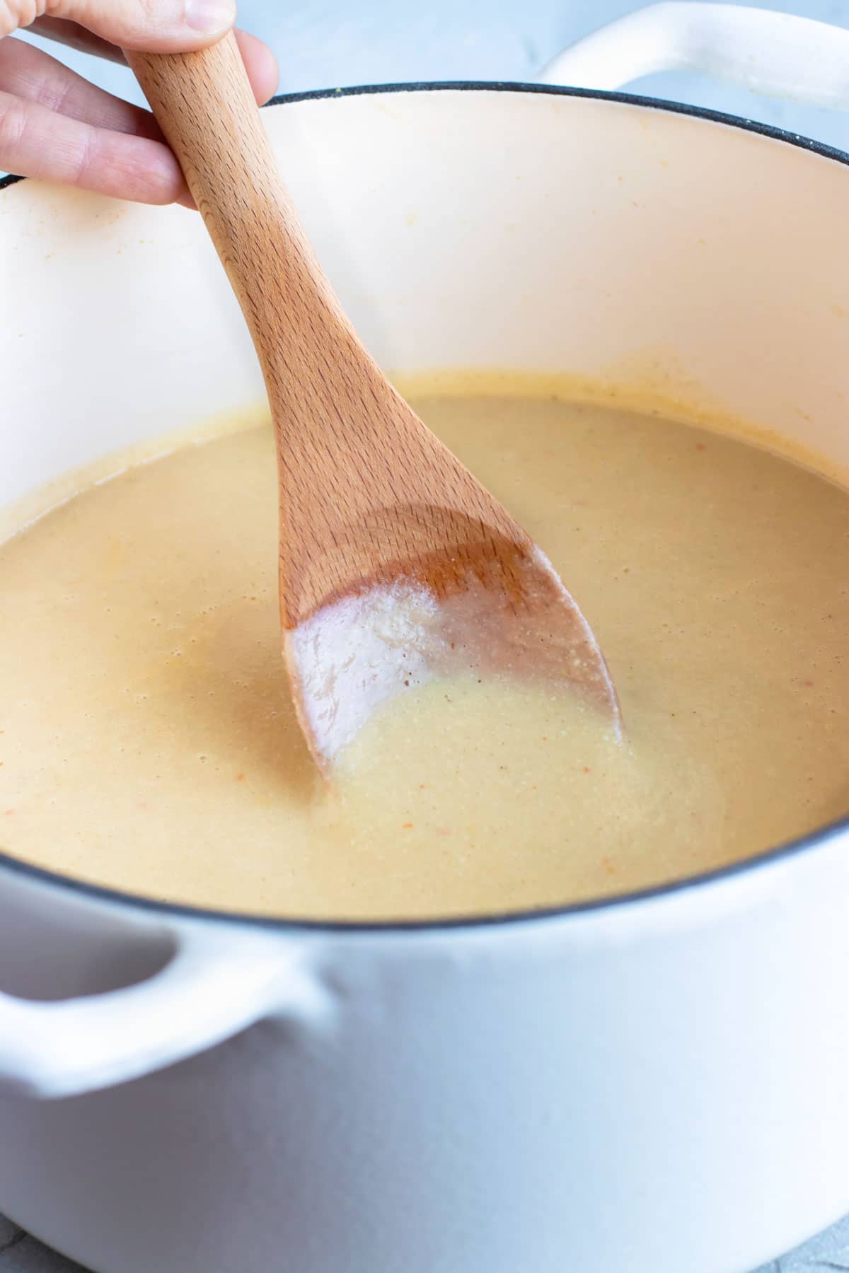 A wooden spoon scooping out creamy cauliflower soup recipe from a Dutch oven.