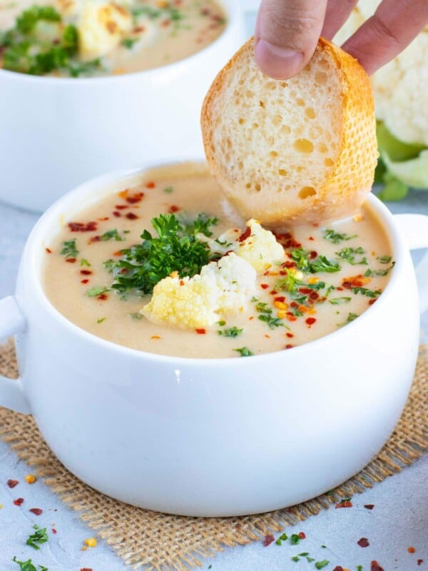 A piece of bread being dunked into a bowl full of vegan cauliflower soup.