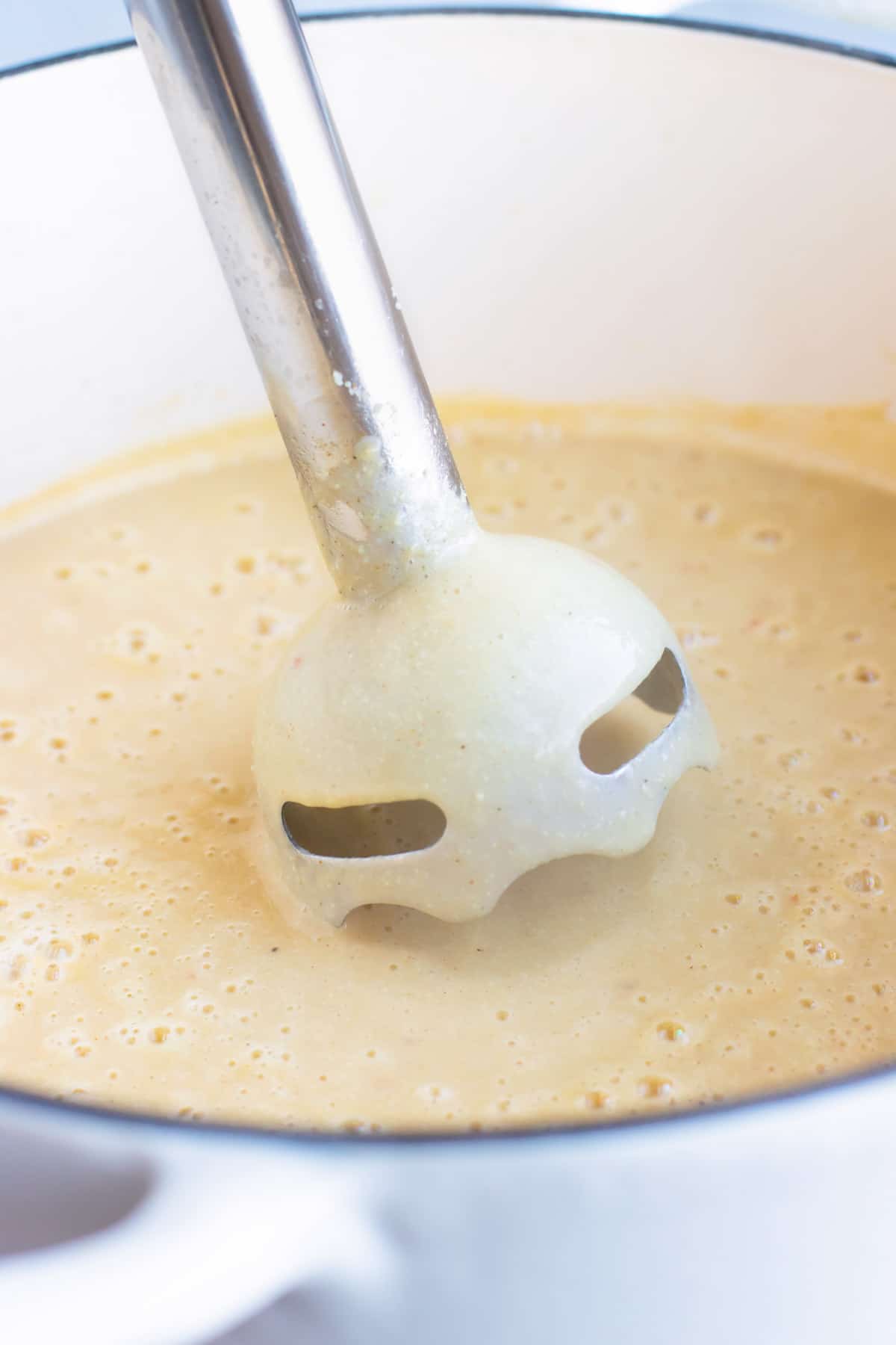 A wand blender going into a pot of cream of cauliflower soup to puree it.