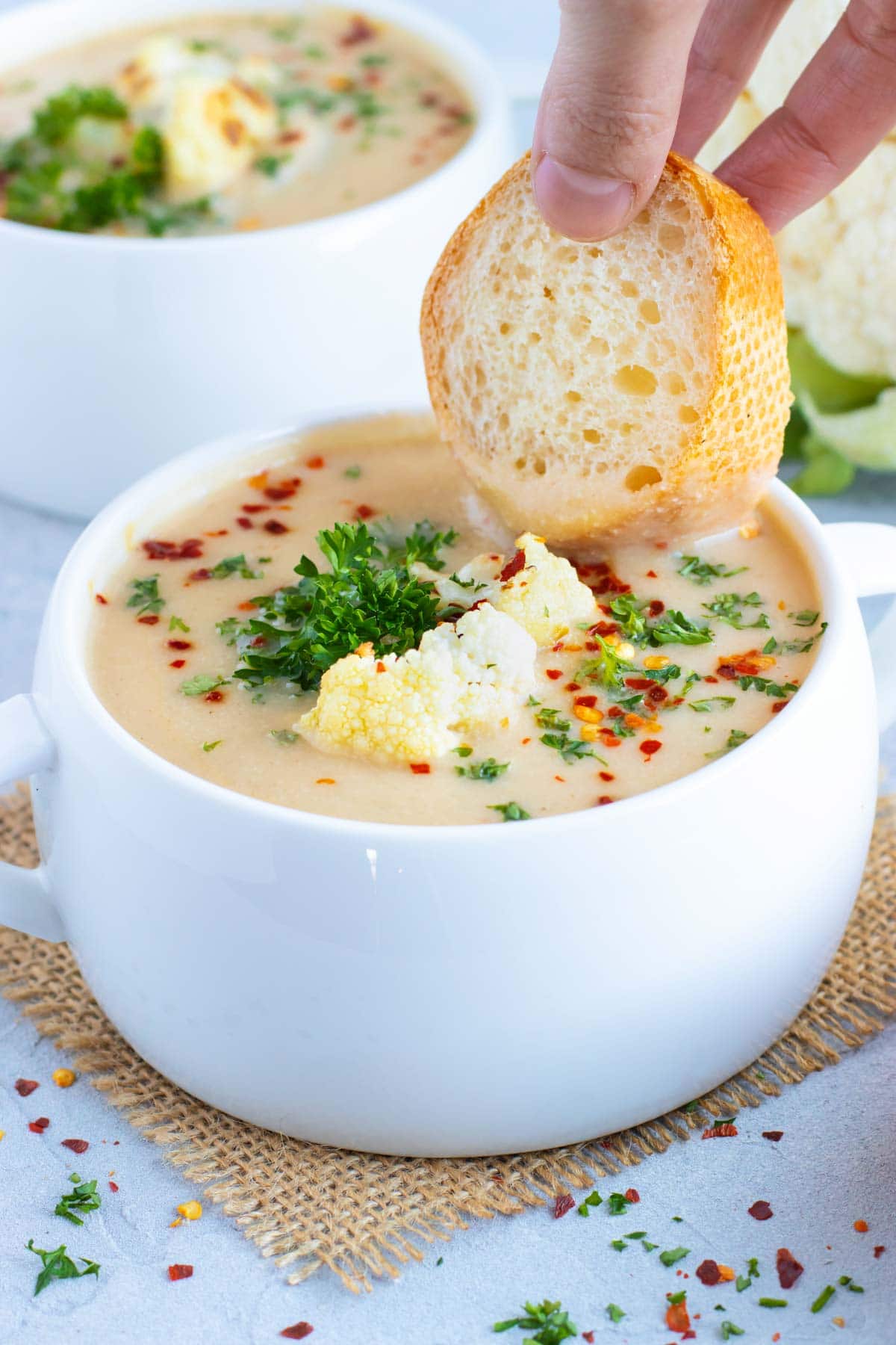 A piece of bread being dunked into a bowl full of vegan cauliflower soup.